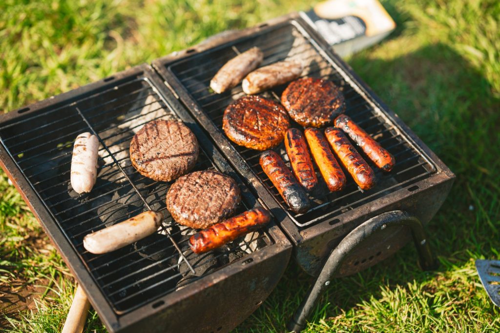 Burgers, sausages and hot dogs grill on a charcoal barbeque in the sunshine.