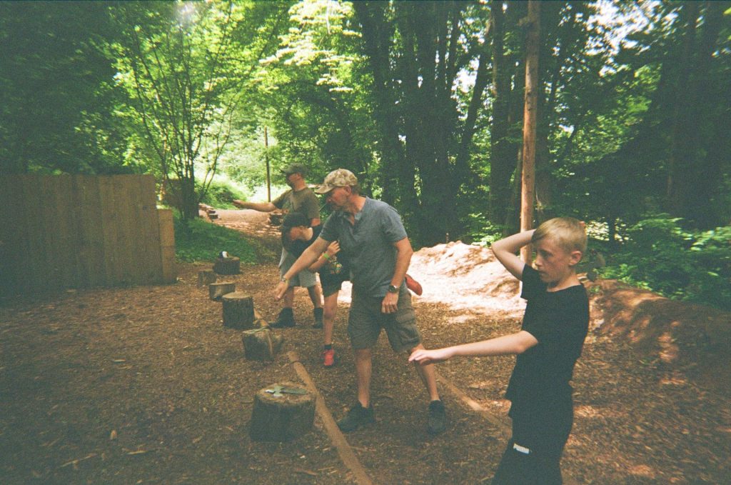Two boys and two men are trying Axe Throwing while on a family camping holiday.