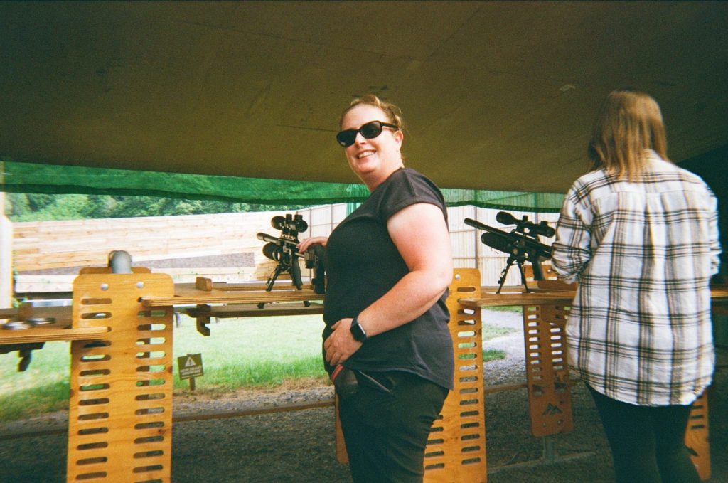 A woman is smiling after taking her turn learning how to use an Air Rifle as part of a 3-day family camping itinerary.