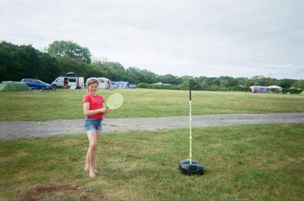 A girl holds a racquet, ready to play a game of swingball that her family brought along to help fill the downtime on their 3 day family camping trip.